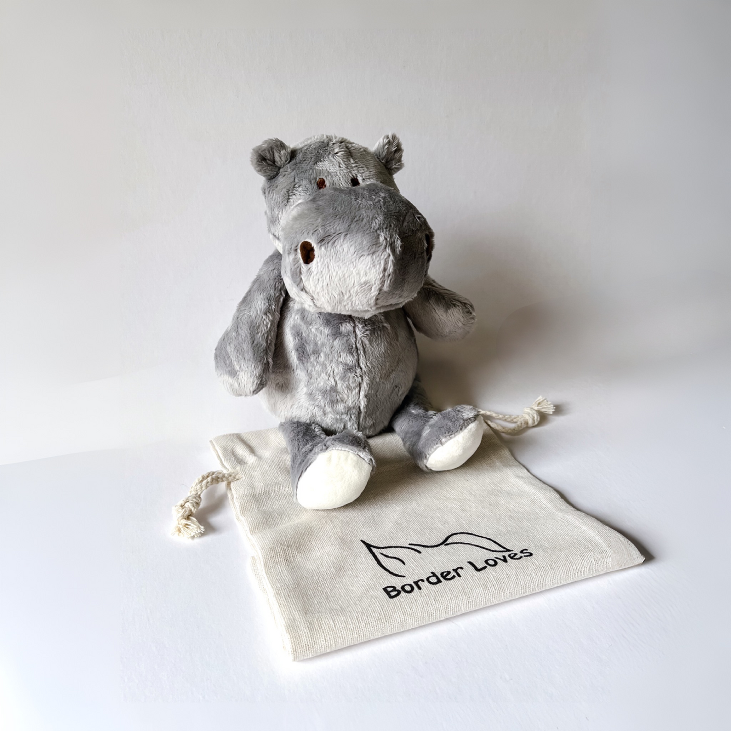 Gray plush hippo dog toy on a white background with a 'Border Loves' drawstring bag.