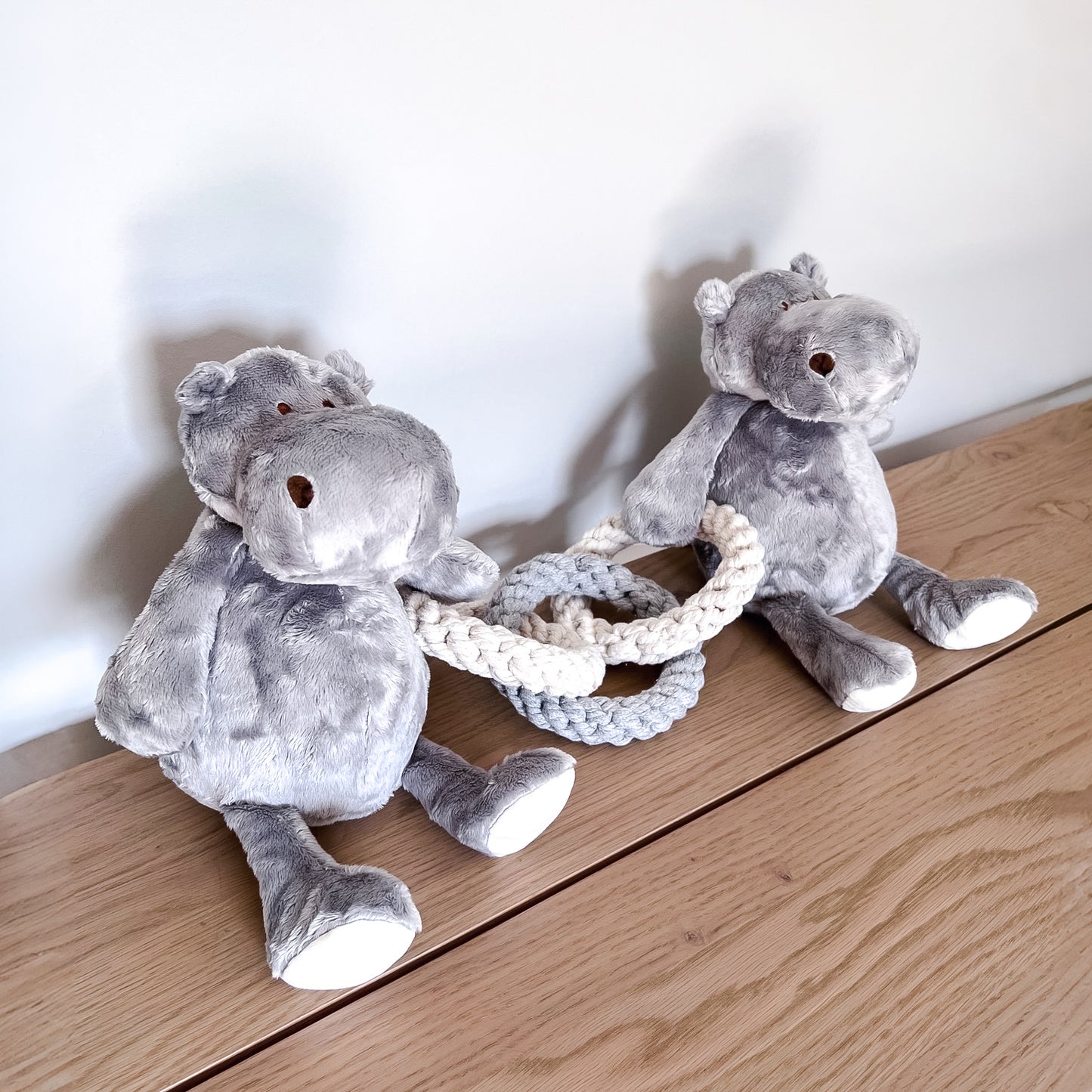 Two gray plush hippo dog toys on a wooden surface with a white background