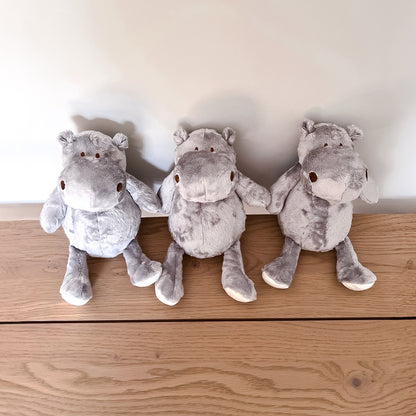 Three grey plush hippopotamuses dog toys lined up on a wooden surface with a white wall in the background.
